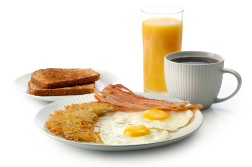 Breakfast with fried eggs, bacon, pancakes and coffee on white table close up. Fried sunny side eggs with bacon on plate and morning cappuccino coffee. American breakfast.