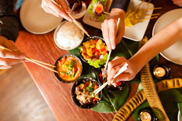 Young people eating in a Thai restaurant, they eating with chopsticks, close-up on hands and food