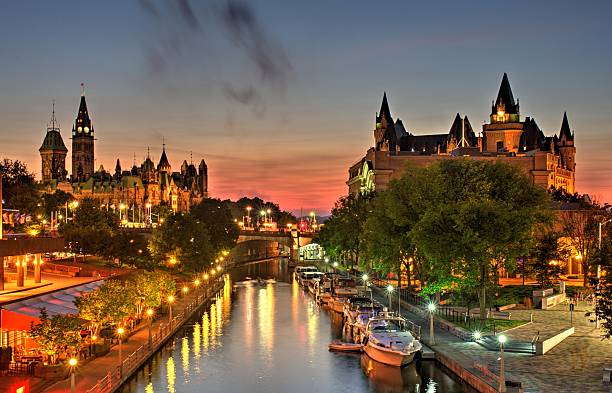 Ottawa Ontario Canada Summer Sunset A beautiful warm orange-red glow fills the sky at dusk over Ottawa Canada during a July evening. A small wisp of low level clouds are visible. Parliament Hill, Chateau Laurier hotel and the Rideau Canal a UNSECO world heritage site are in the foreground.   parliament hill ottawa stock pictures, royalty-free photos & images