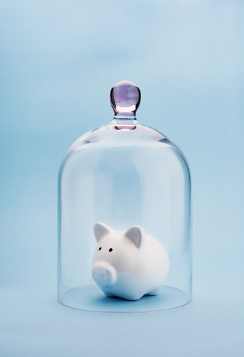 Piggybank protected under a glass dome on blue background