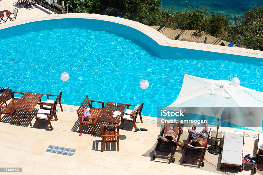 View of a couple sitting on deck chairs enjoying vacation View of a couple sitting on deck chairs enjoying vacation near swimming pool Adult Stock Photo