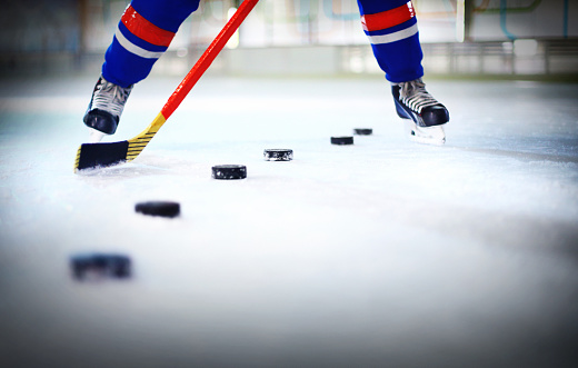 Unrecognizable ice hockey player shooting many pucks one after another. He's using red hockey stick, wearing red and blue hockey socks.Low angle view.Vignette.