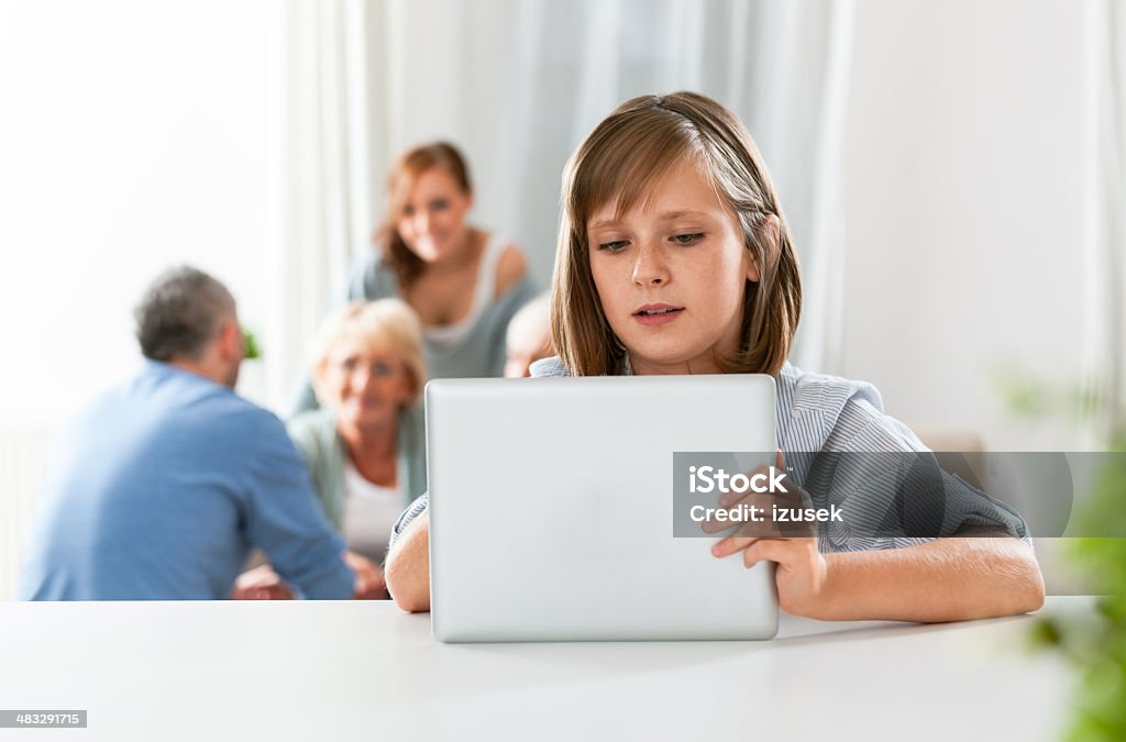 Cute girl with digital tablet Girl using a digital tablet at home with her parents and grandparents in the background. Adult Stock Photo
