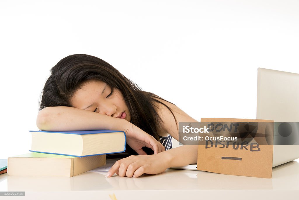 young pretty chinese asian student tired asleep on laptop young pretty chinese woman student asleep on computer and textbooks from being overworked after studying for exam with a don't disturb sign on her desk on a white background Adult Stock Photo