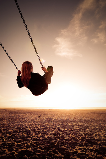 Cross processed image of a woman on a swing at the beach just before sunset with vignettes and lens flare.