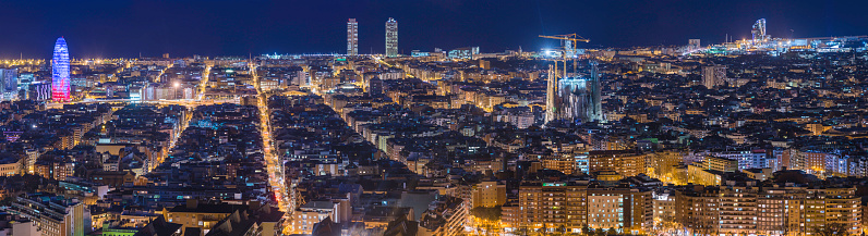 Lights illuminating the iconic spires of the Sagrada Familia, crowded downtown avenues and Mediterranean coastline landmarks in this dramatic night panorama of Barcelona, Spain. ProPhoto RGB profile for maximum color fidelity and gamut.