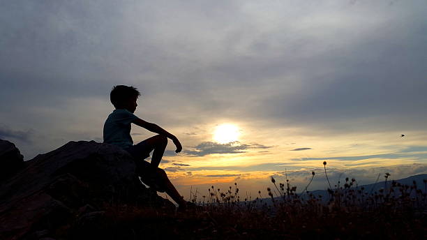 Sunset Child Silhouette Relaxed boy on hill. religion sunbeam one person children only stock pictures, royalty-free photos & images