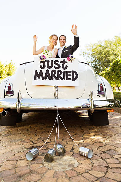 les jeunes mariés agitant dans une voiture décapotable avec boîtes attenante - just married photos et images de collection