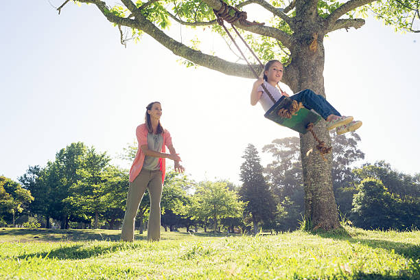istock Mother pushing daughter on swing at park 483315773