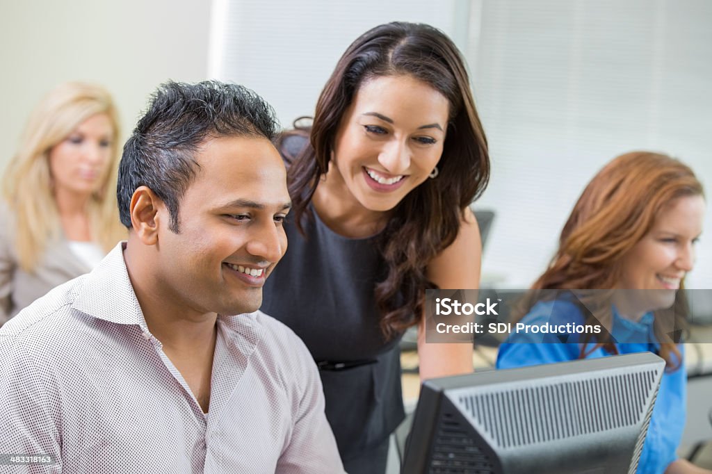 Teacher assisting man with computer during corporate training class Education Training Class Stock Photo