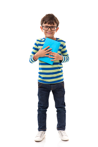 Schoolboy stands in front of a white background and holds a blue book.
