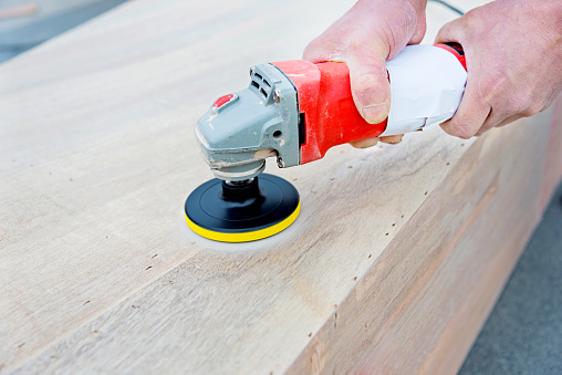 Man holding a buffing machine on wood counter.