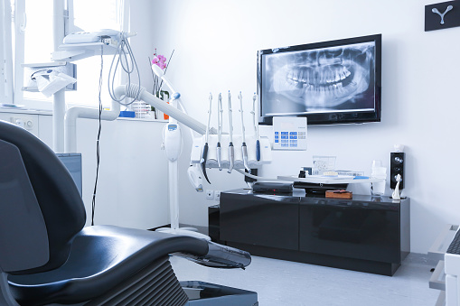 Dentists chair and tools with x-ray picture on TV in the background. Dental care, dental hygiene, checkup and therapy concept.