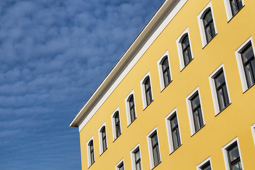 Diagonal view on a traditional house with a new facade in yellow color and contrast white details. Blue sky in the background with many small clouds.