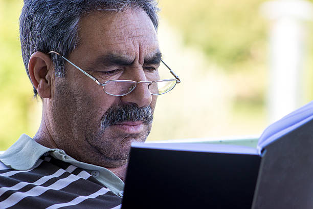 Serious senior man reading a novel Serious senior man reading a novel. Close-up portrait of a senior adult man. He is looking at book seriously. Horizontal composition. Image developed from Raw. middle eastern ethnicity mature adult book reading stock pictures, royalty-free photos & images