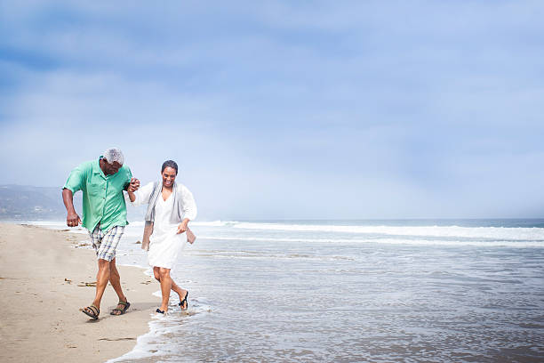 African American Seniors Walking on Beach Senior African American couple walking on the beach, running from the waves lypsela2013 stock pictures, royalty-free photos & images