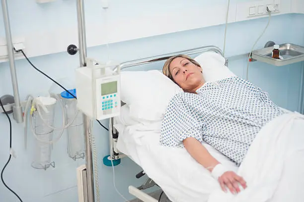Female patient lying on a medical bed with halfclosed eyes in hospital ward