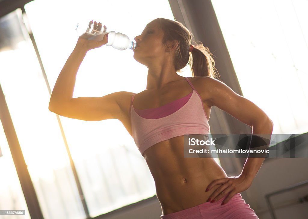 Drinking water Muscular woman posing and drinking water in gym after workout. 20-29 Years Stock Photo