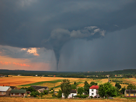 View of the serene countryside and stormy sky with a tornado in the background.