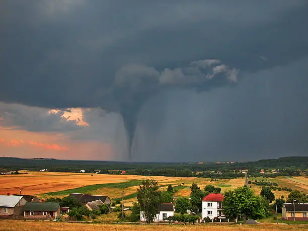 View of the serene countryside and stormy sky with a tornado in the background.