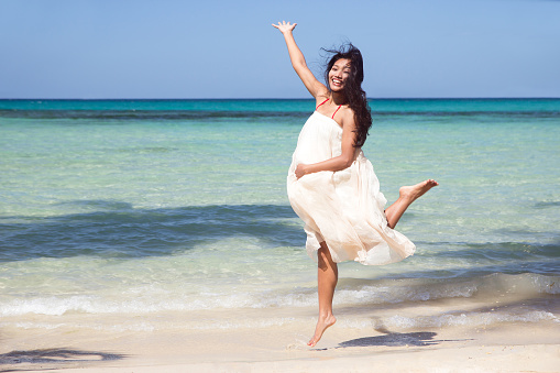 cheerful pregnant woman jumping on the beach