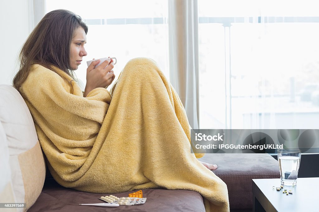 Side view of sick woman having coffee Side view of sick woman having coffee on sofa in living room 20-24 Years Stock Photo