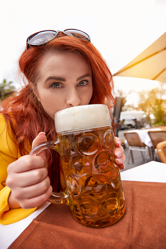 wide angle lens on woman portrait drinking big mug of beer, photo taken on outdoor terrace.