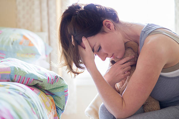 Greiving A grieving mother sits in her child's bedroom holding their toy in her arms while resting her head in her hands. The child's bed can be seen in the background untouched from when they were last in it. woman defeat stock pictures, royalty-free photos & images