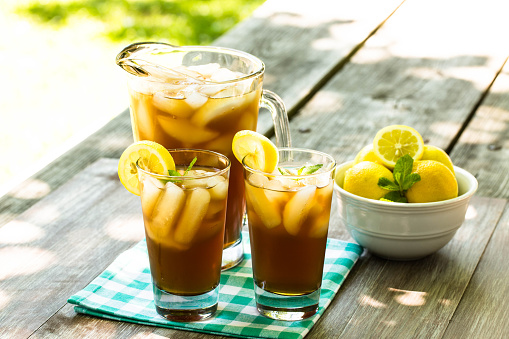 Two glasses and pitcher of iced tea with lemons on picnic table