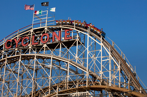 Coney Island, New York, USA - July 11, 2015: People riding the famous Cyclone wooden roller coaster  onthe first or main drop in Coney Island, Brooklyn, New York City on a summer day. The Cyclone was declared a New York City landmark on July 12, 1988, and was placed on the National Register of Historic Places on June 26, 1991.