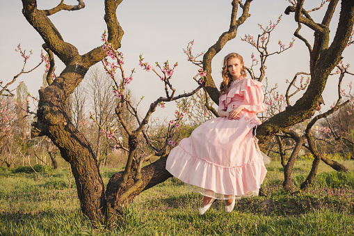 Fairytale woman sitting on the big tree branch in the pink dress