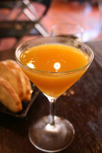 Mango cocktail, bright orange color, made with mango puree, on a dark wooden table, with slices of sourdough bread