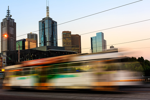 A tram passing by the city center of Melbourne in Australia at dusk. The tram is blurred due to motion and long exposure.