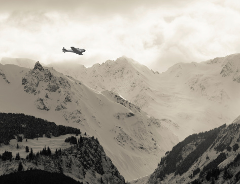 Vintage WWII airplane flying over mountain peaks in Southeast Alaska.