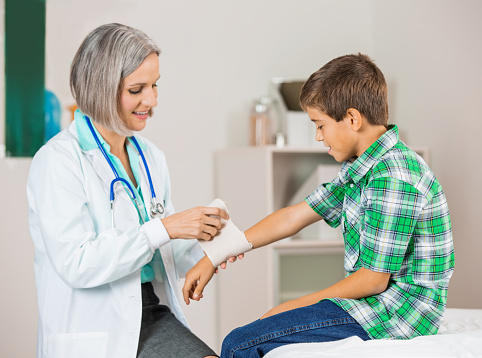 Friendy doctor wrapping injured wrist of young patient