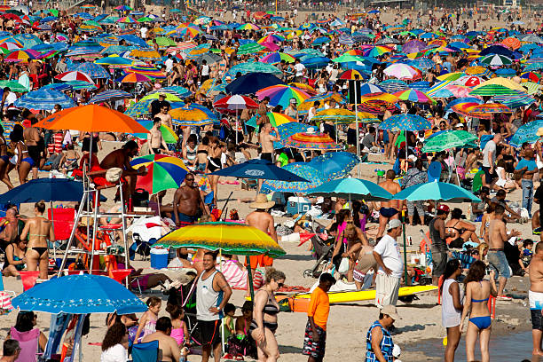 Coney Island, New York, USA - July 11, 2015: Beach crowded with sunbathers and swimmers in Coney Island on a warm summer day in July. Coney Island is a popular summer time vacation destination and local retreat for New Yorkers.
