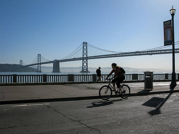 radfahrer und bay bridge in san francisco - san francisco county embarcadero center bay bridge built structure stock-fotos und bilder