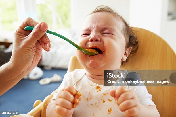 Unhappy Baby Being Fed In High Chair At Meal Time Stock Photo - Download Image Now - Baby - Human Age, Feeding, Messy