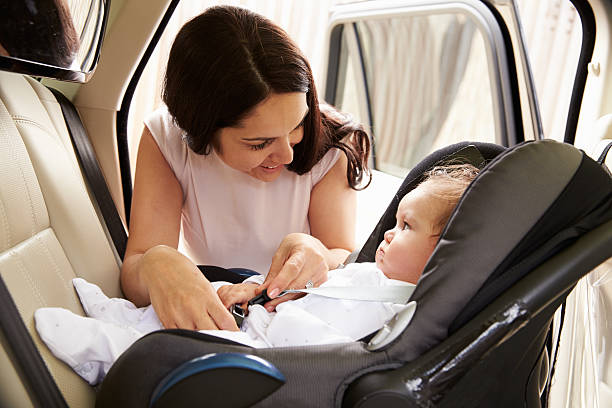 mother putting baby son into car travel seat - 嬰兒安全座椅 圖片 個照片及圖片檔