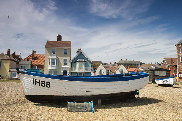 Aldeburgh, Suffolk, UK - August 5, 2015: blue and white wooden boats on Aldeburgh beach with some of the town's colourful seafront houses as a backdrop, under a pretty August sky.