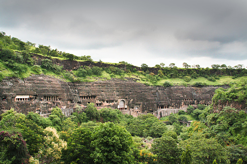 A series of ancient historic Buddhist Cave Temples. Caved into the side of the mountain in Arrangabad, in the Indian state of Maharashtra. India. A UNESCO World Heritage Site, and one of the major tourist destination in the region. Photographed on location outside the cave site in Ajanta in horizontal format.