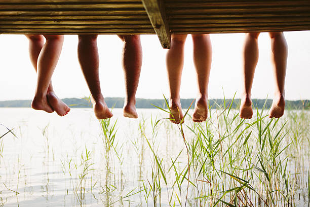 istock Legs of four young adults sitting on a jetty 483442942