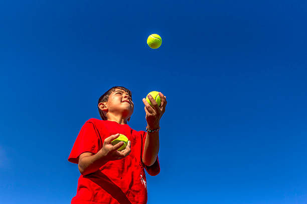 Young boy juggles balls. A young boy tries juggling against a bright blue sky. juggling stock pictures, royalty-free photos & images