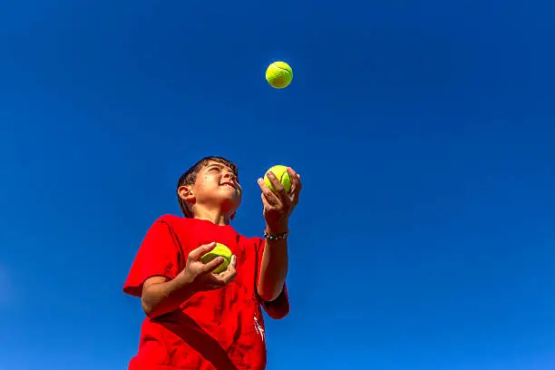 A young boy tries juggling against a bright blue sky.