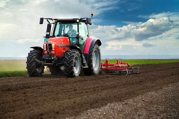 Photo of Close-up of agriculture red tractor cultivating field over blue sky