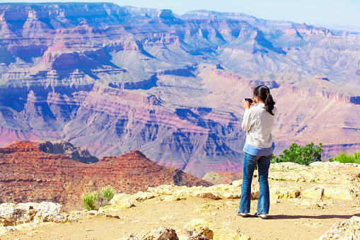 Teen girl taking pictures at the Grand Canyon with cell phone.