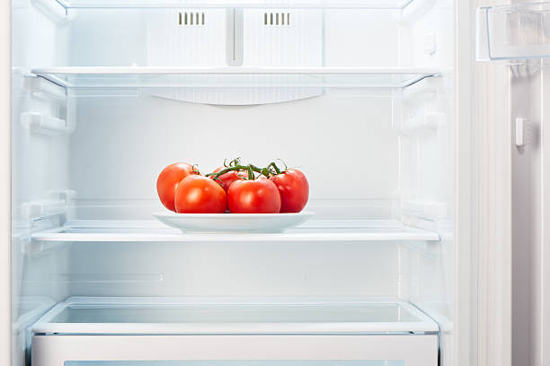 Branch of tomatoes on white plate in open empty refrigerator