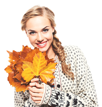 Portrait of happy blonde young woman wearing woolen sweater holding autumn leaves, smiling at camera. Studio shot, isolated on white.