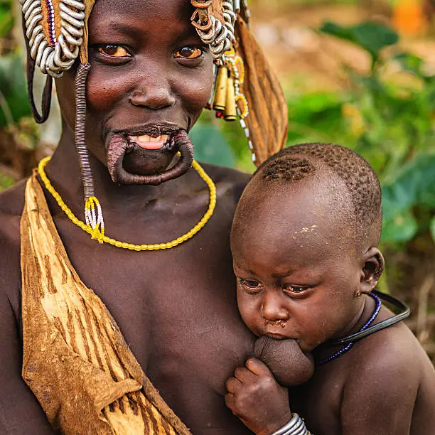 Woman from Mursi tribe breastfeeding her baby.  Mursi tribe are probably the last groups in Africa amongst whom it is still the norm for women to wear large pottery or wooden discs or ‘plates’ in their lower lips.http://bem.2be.pl/IS/ethiopia_380.jpg