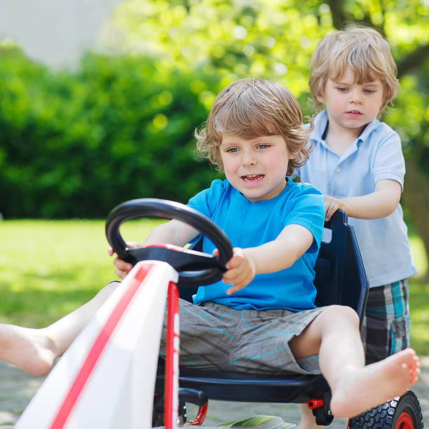 dos divertidos niños divirtiéndose con coches de carrera al aire libre - car child teamwork sports race fotografías e imágenes de stock